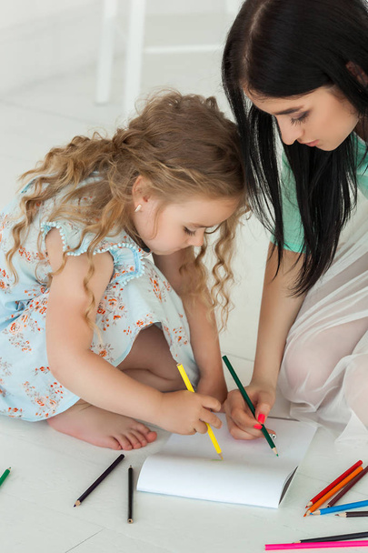 Little cute daughter and her mother drawing with colorful pencil - Photo, Image