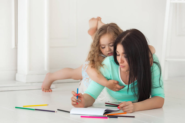 Little cute daughter and her mother drawing with colorful pencil - Foto, imagen