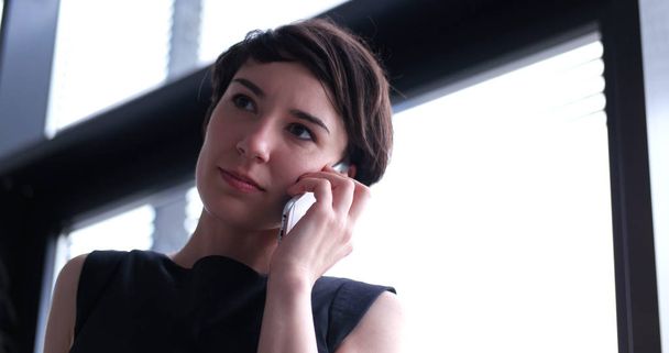 businesswoman speaking on phone beside window of modern office   - Фото, зображення