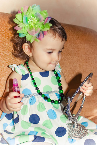 Beautiful little girl looking in the mirror and paints her lips. Selective focus.  - Photo, Image