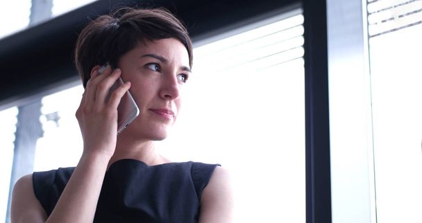 businesswoman speaking on phone beside window of modern office   - Foto, immagini