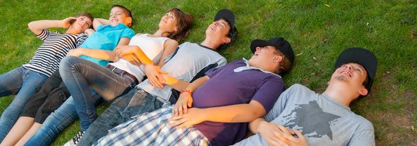 Adolescentes niños y niñas tumbados en la hierba en el hermoso día soleado de primavera
 - Foto, Imagen