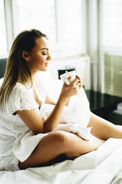 Mulher sentada em uma cama com café
 - Foto, Imagem