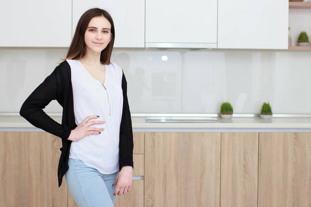 hübsche junge Frau mit schwarzen Haaren, die in der Küche steht und lächelt - Foto, Bild