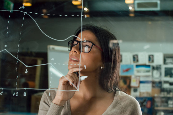 Young attractive female thinking near glass whiteboard - Foto, afbeelding