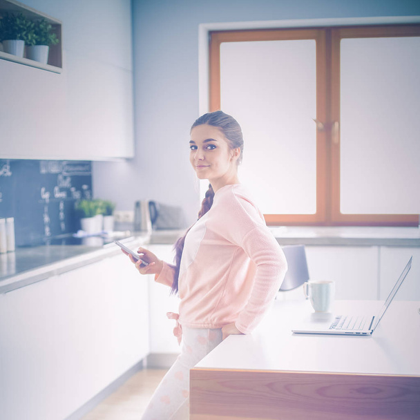 Woman using mobile phone standing in modern kitchen - Foto, afbeelding