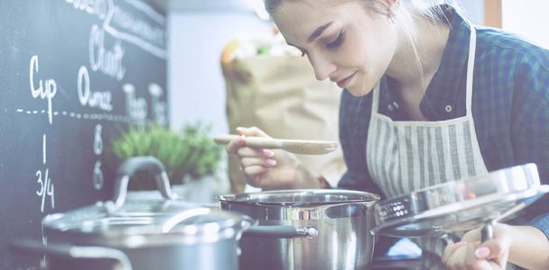 Young woman cooking in her kitchen standing near stove - Foto, imagen