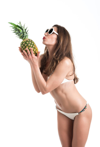 Portré fiatal egészséges gyönyörű nő fehér bikini és fehér napszemüveg, a kéz friss ananász - Fotó, kép