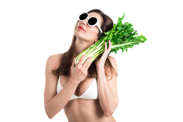 Retrato de mujer joven sana en bikini blanco y gafas de sol blancas con achicoria fresca en una mano
. - Foto, Imagen