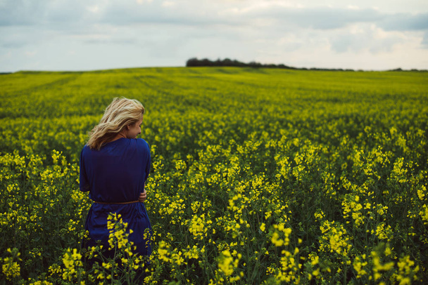 Woman standing in rapeseed field. Windy weather. - Φωτογραφία, εικόνα