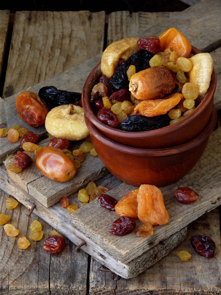 A composition from different varieties of dried fruits on a wooden background - dates, figs, apricots, prunes, raisins, cranberries. Healty food - Photo, Image