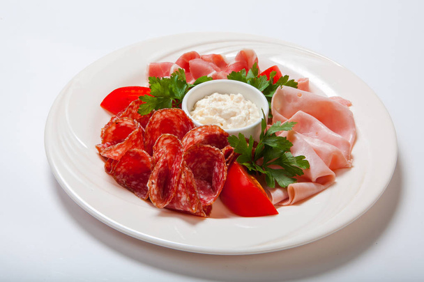 Cold smoked meat plate with prosciutto, salami, bacon, ham and sauce on a white plate. - Фото, зображення