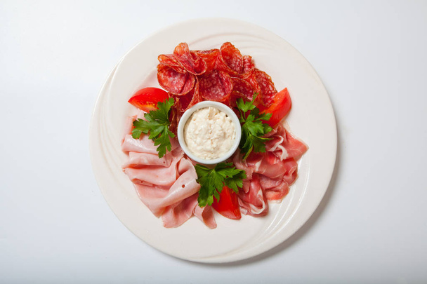 Cold smoked meat plate with prosciutto, salami, bacon, ham and sauce on a white plate. - Photo, image