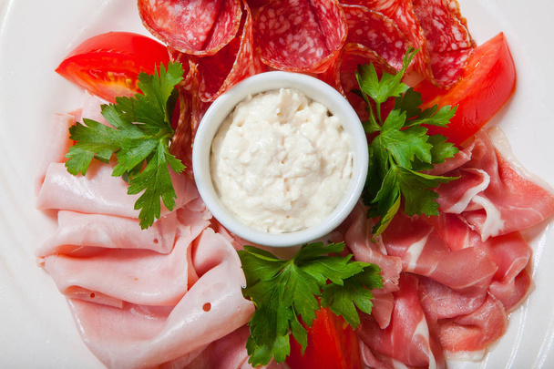 Cold smoked meat plate with prosciutto, salami, bacon, ham and sauce on a white plate. - Photo, image