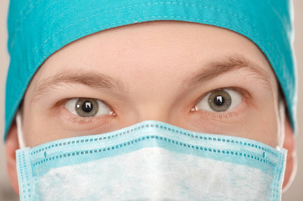 αρσενικό χειρουργός στη μάσκα που βλέπουν τα φωτογραφικών μηχανών σε γκρίζο φόντο, κοντινό πλάνο - Φωτογραφία, εικόνα