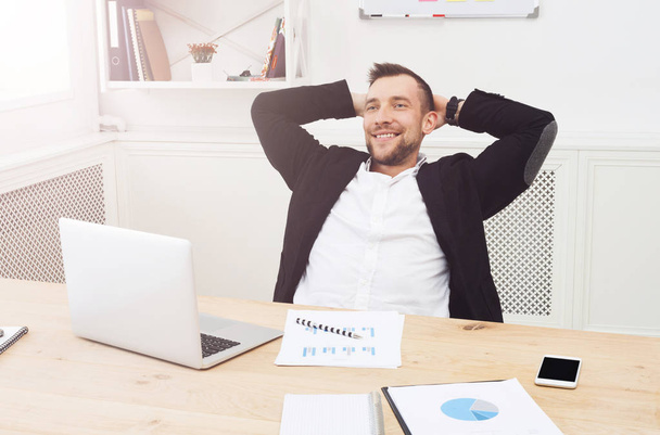 junger entspannter Geschäftsmann mit Laptop im modernen weißen Büro - Foto, Bild
