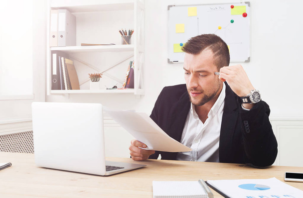 Jovem empresário concentrado ler documentos no escritório branco moderno
 - Foto, Imagem