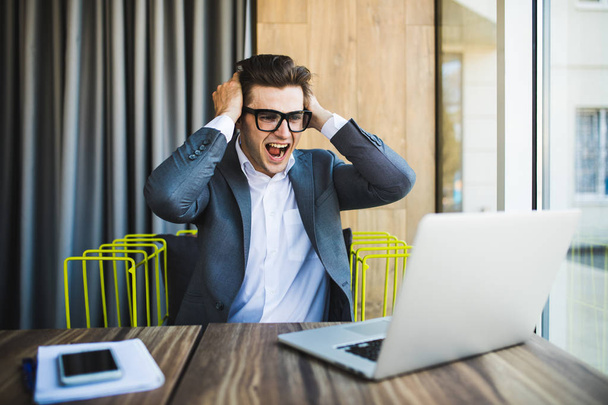 Happy businessman in glasses failure with raised fists on head and screaming look at laptop - Foto, Bild