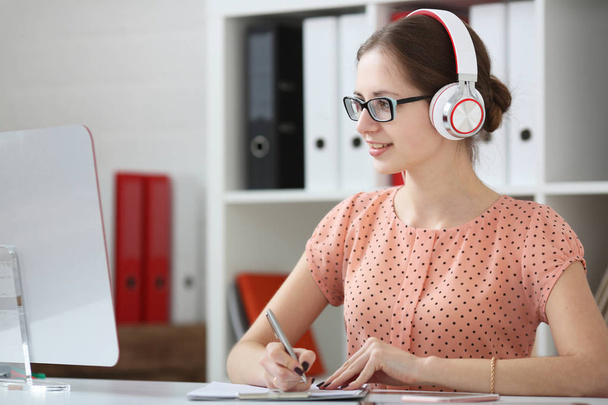 Female student with headphones listening to music and learning. Hold the handle in his hand and looking at monitor - Foto, imagen