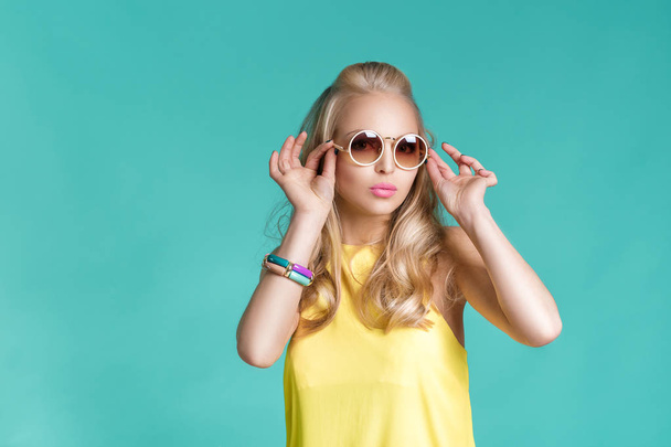 portrait of beautiful blond woman in sunglasses and yellow shirt on blue background. Carefree summer. - Fotó, kép
