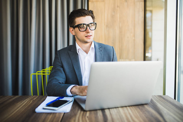 Красивий бізнесмен в окулярах працює з ноутбуком в офісі
 - Фото, зображення