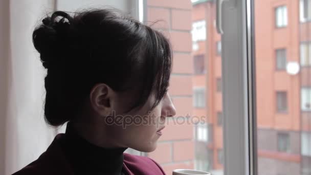 Brunette drinken koffie en kijken uit het raam - Video