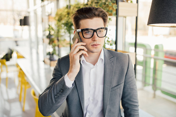 Smiling businessman sitting and using mobile phone in office - Foto, afbeelding