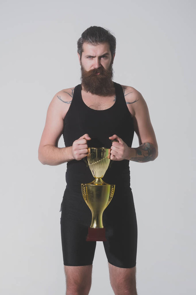 vousatý muž vážné drží zlatý pohár šampionů na šedém pozadí - Fotografie, Obrázek