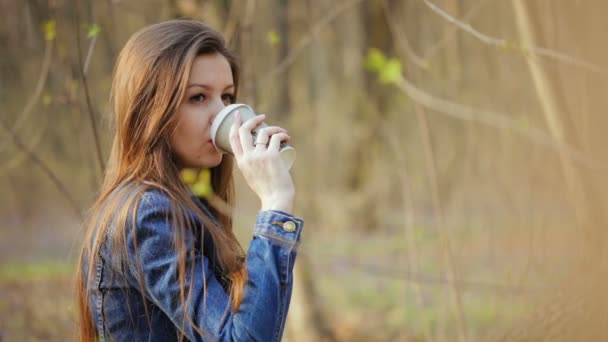 Young woman drinks a hot drink out of paper cup - Footage, Video
