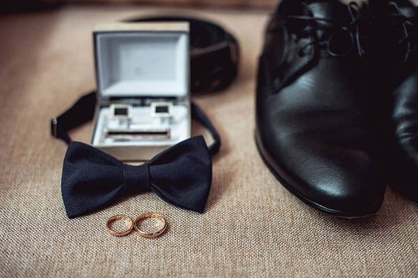 Primer plano de los accesorios de hombre moderno. anillos de boda, corbata negra, zapatos de cuero, cinturón y gemelos
 - Foto, Imagen