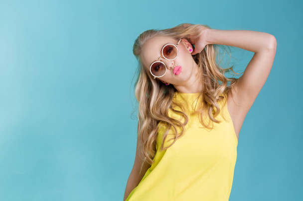 portrait of beautiful blond woman in sunglasses and yellow shirt on blue background. Carefree summer. - Foto, Imagem