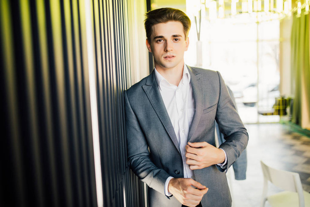 Successful businessman dressed in expensive suit is standing in hallway his company. Young male manager is posing in modern office - Фото, зображення