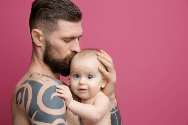 Handsome tattooed young man holding cute little baby on color background - Foto, Imagen
