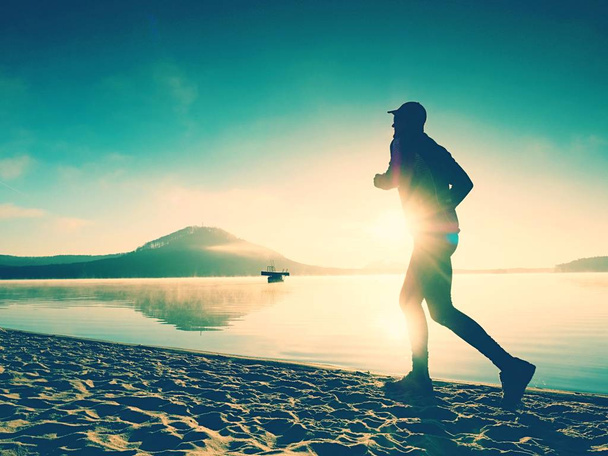 Silueta del hombre activo deportivo corriendo en la playa del lago al amanecer. Estilo de vida saludable
.  - Foto, imagen