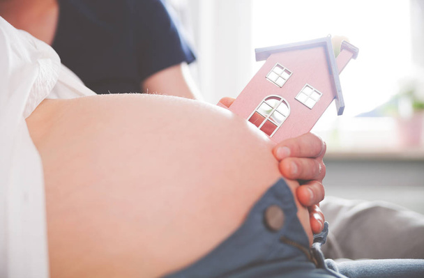 Close up of pregnant belly with small house, concept of new home and familiy - Fotografie, Obrázek