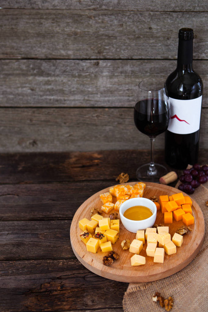 Trauben, Käse, Feigen und Honig mit einer Flasche und einem Glas Rotwein - Foto, Bild