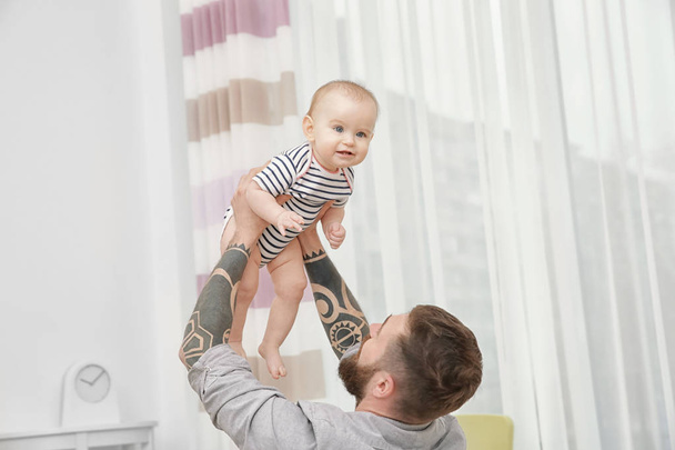 Handsome tattooed young man playing with cute little baby at home - Fotoğraf, Görsel