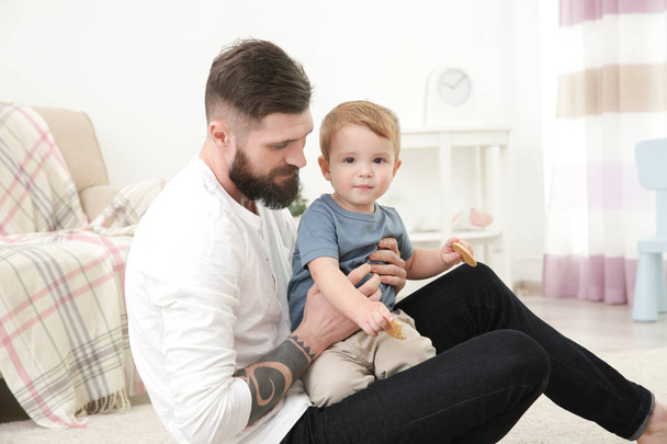 Handsome tattooed young man playing with cute little boy at home - Foto, Bild