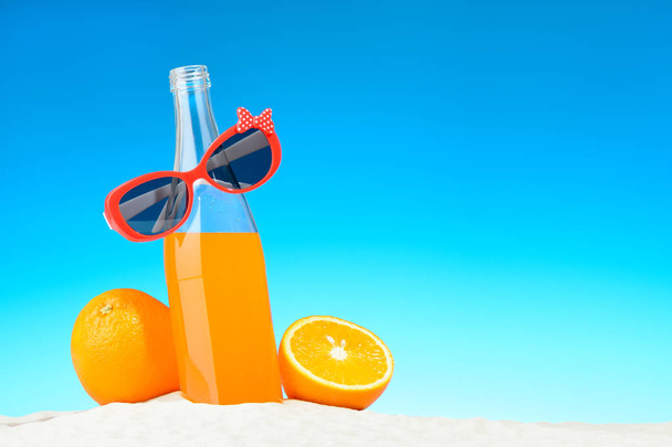 Бутылка апельсинового сока и солнцезащитные очки на пляже
 - Фото, изображение