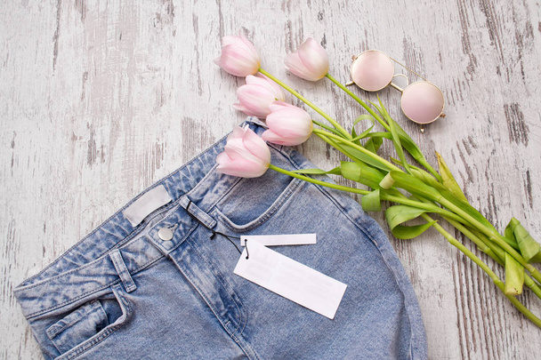 Jeans avec une étiquette propre, lunettes roses et tulipes sur un fond en bois. Concept à la mode, vue de dessus
 - Photo, image