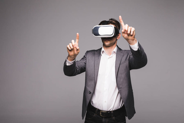 Portrait of man in a suit with virtual reality glasses on his head pointed with hand isolated on grey background. - Фото, изображение