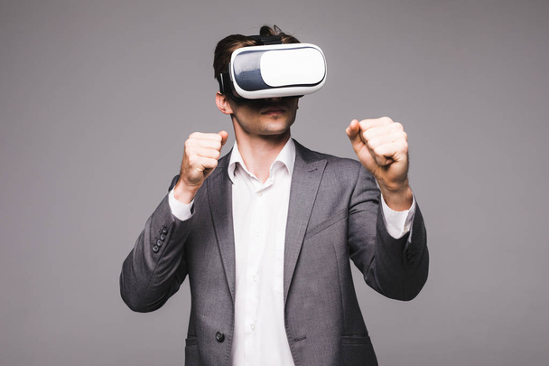 Man in een pak met virtual reality bril op zijn hoofd boksen geïsoleerd op een grijze achtergrond. - Foto, afbeelding