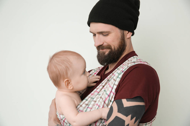 Handsome tattooed young man holding cute little baby on light background - Fotoğraf, Görsel