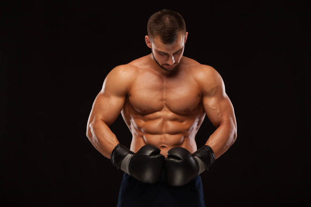 Muscular young man with perfect Torso with six pack abs, in boxing gloves is showing the different movements and strikes isolated on black background with copyspace - Photo, image