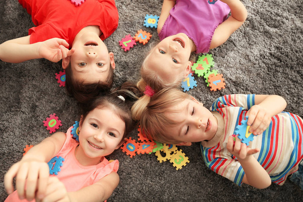 Cute little children playing with colorful figures while lying on carpet at home - Foto, imagen
