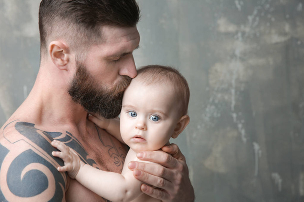 Handsome tattooed young man holding cute little baby on gray background - Foto, Imagen