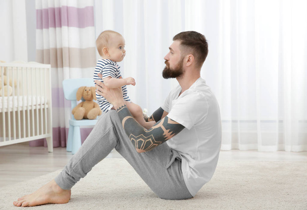 Handsome tattooed young man playing with cute little baby at home - Photo, Image