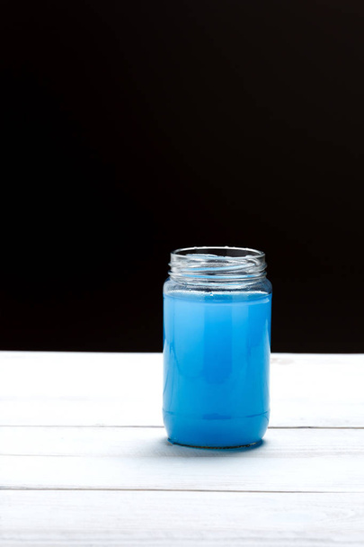 Glass jar with a liquid of blue color on black and white background - Foto, imagen
