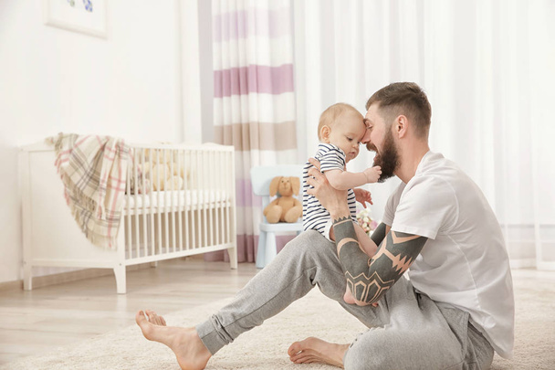 Şirin bebek ile evde oynarken dövmeli yakışıklı genç - Fotoğraf, Görsel