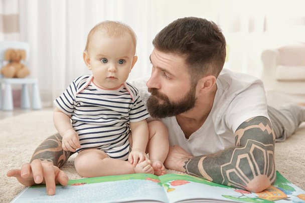 Handsome tattooed young man playing with cute little baby at home - Foto, immagini